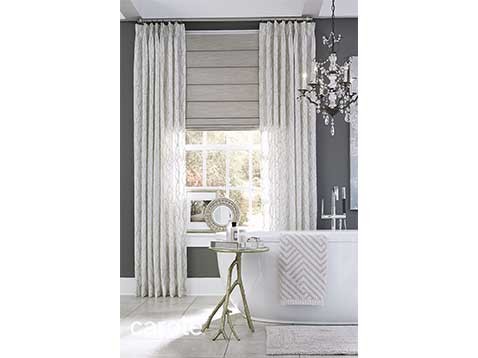A bathroom with a tub, glass chandelier, and a large window with white drapes